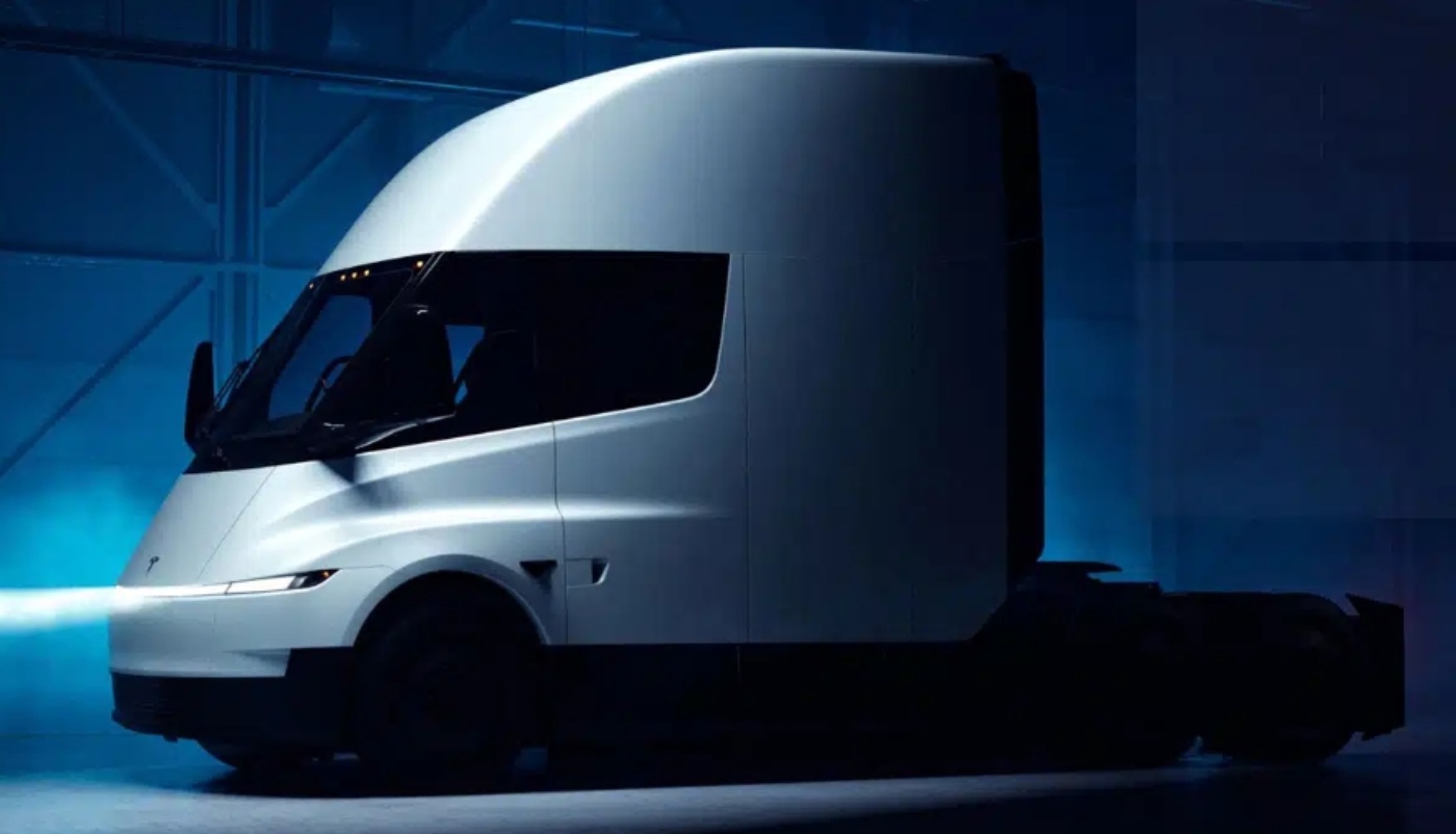 A white electric semi-truck is shown in a dark studio with dramatic lighting.