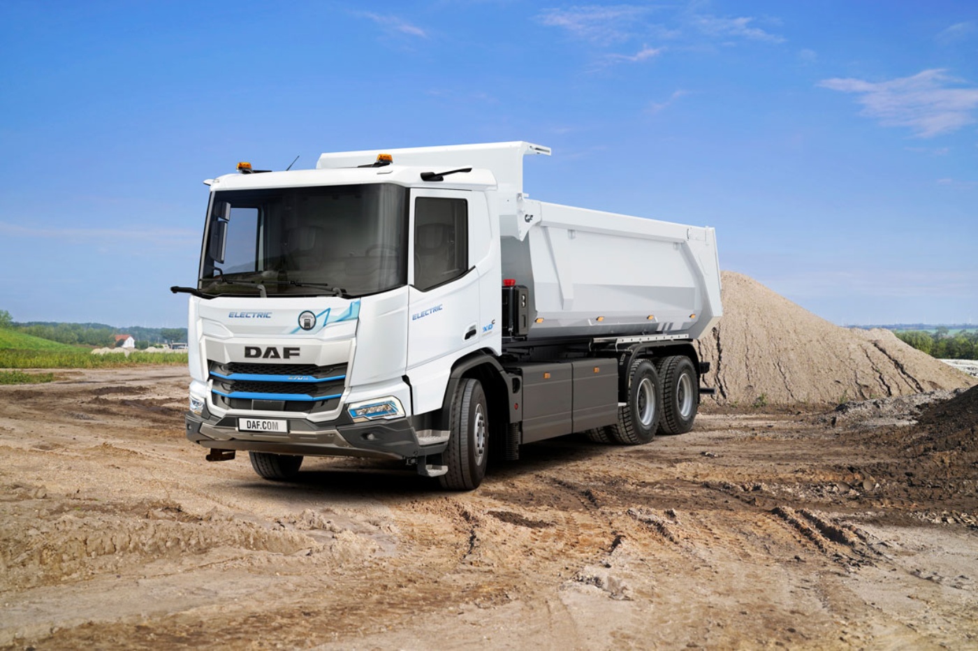A white DAF electric dump truck is parked on a construction site with soil piles.