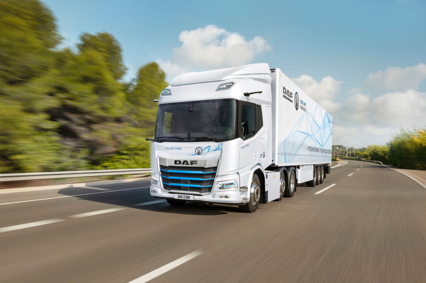 A white DAF electric truck is driving on a curved highway surrounded by greenery.
