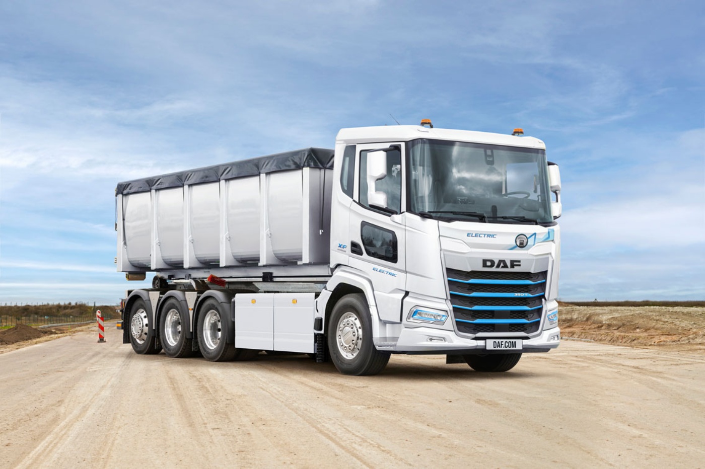 A white DAF electric truck with covered trailer is parked on a dirt road under blue sky.