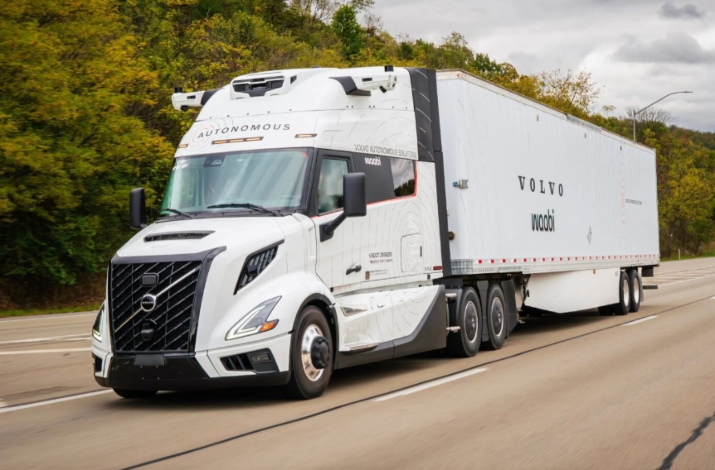 A white autonomous Volvo truck with Waabi branding drives on a highway near trees.