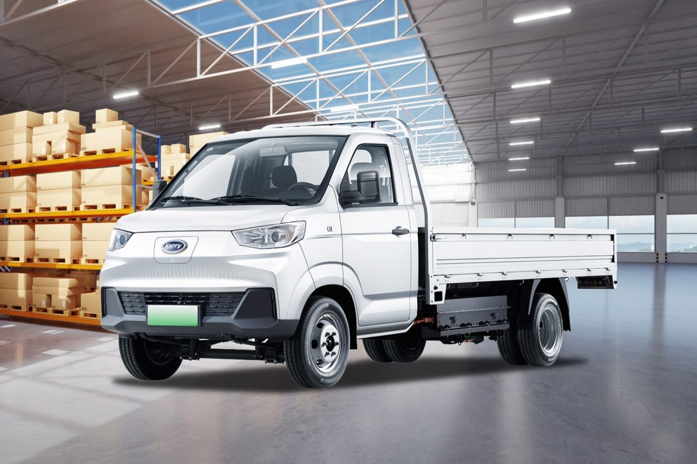 A white Karry electric flatbed truck is parked inside a warehouse near stacked boxes.