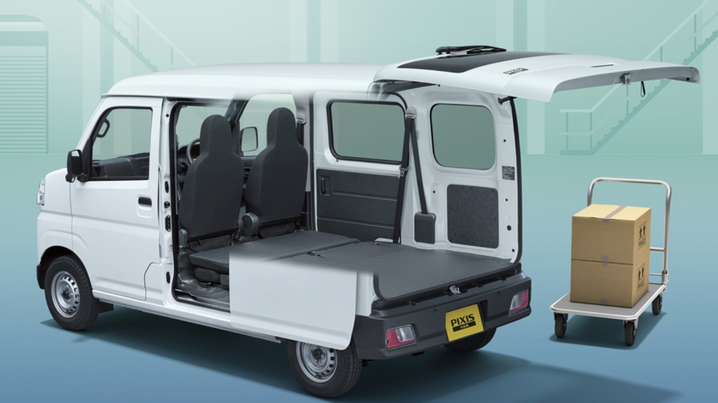 Small van with open rear and side doors shows flat cargo space next to a trolley with boxes.