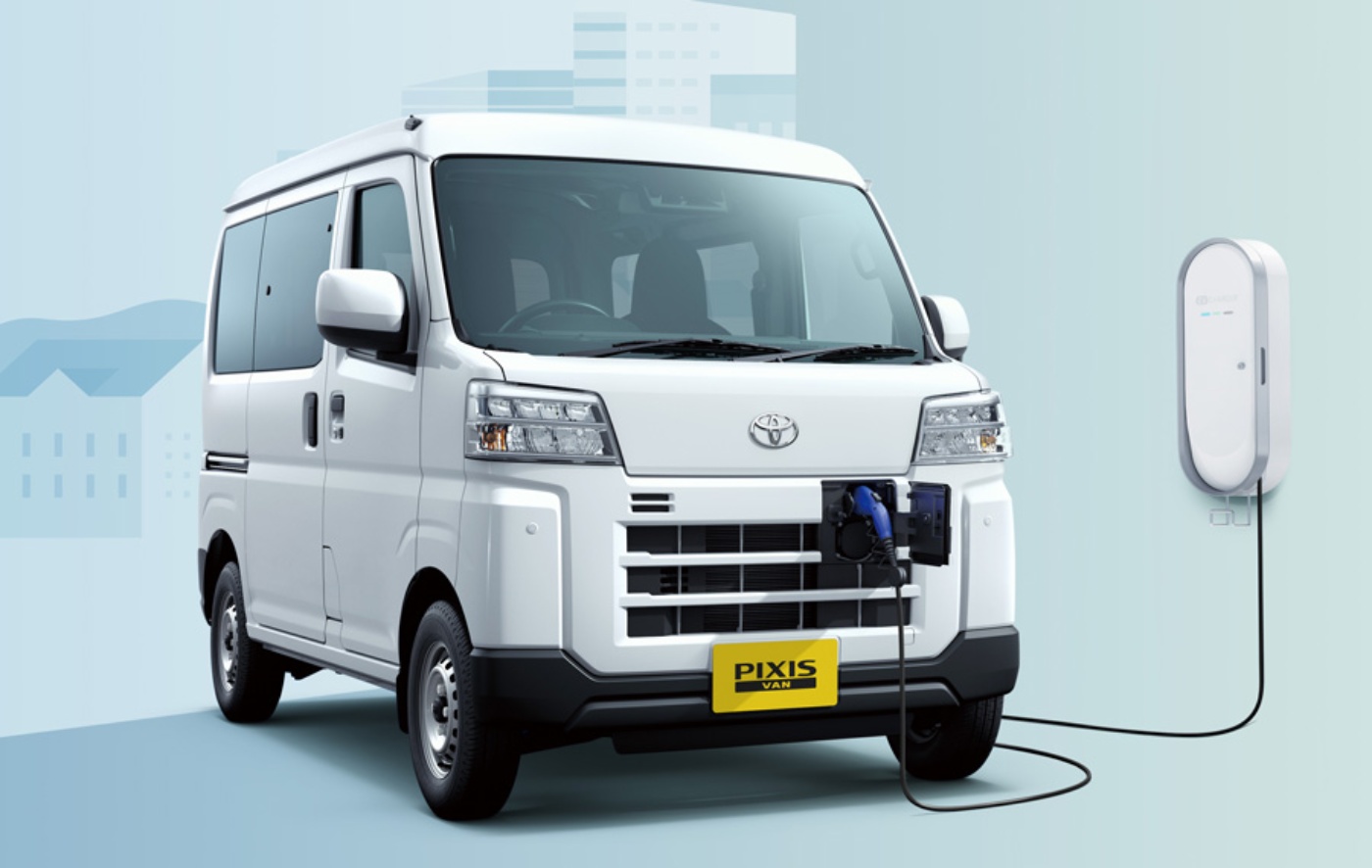 Elektro-Van mit „Pixis Van“-Logo lädt vorne an einer wandmontierten Ladestation.