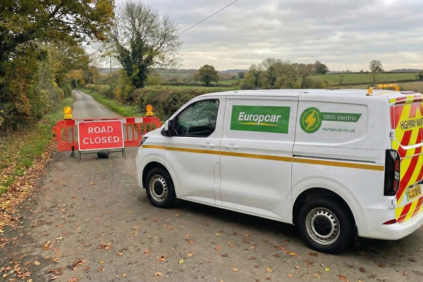 Electric Europcar van parked in front of a roadblock with a "Road Closed" sign in the countryside.