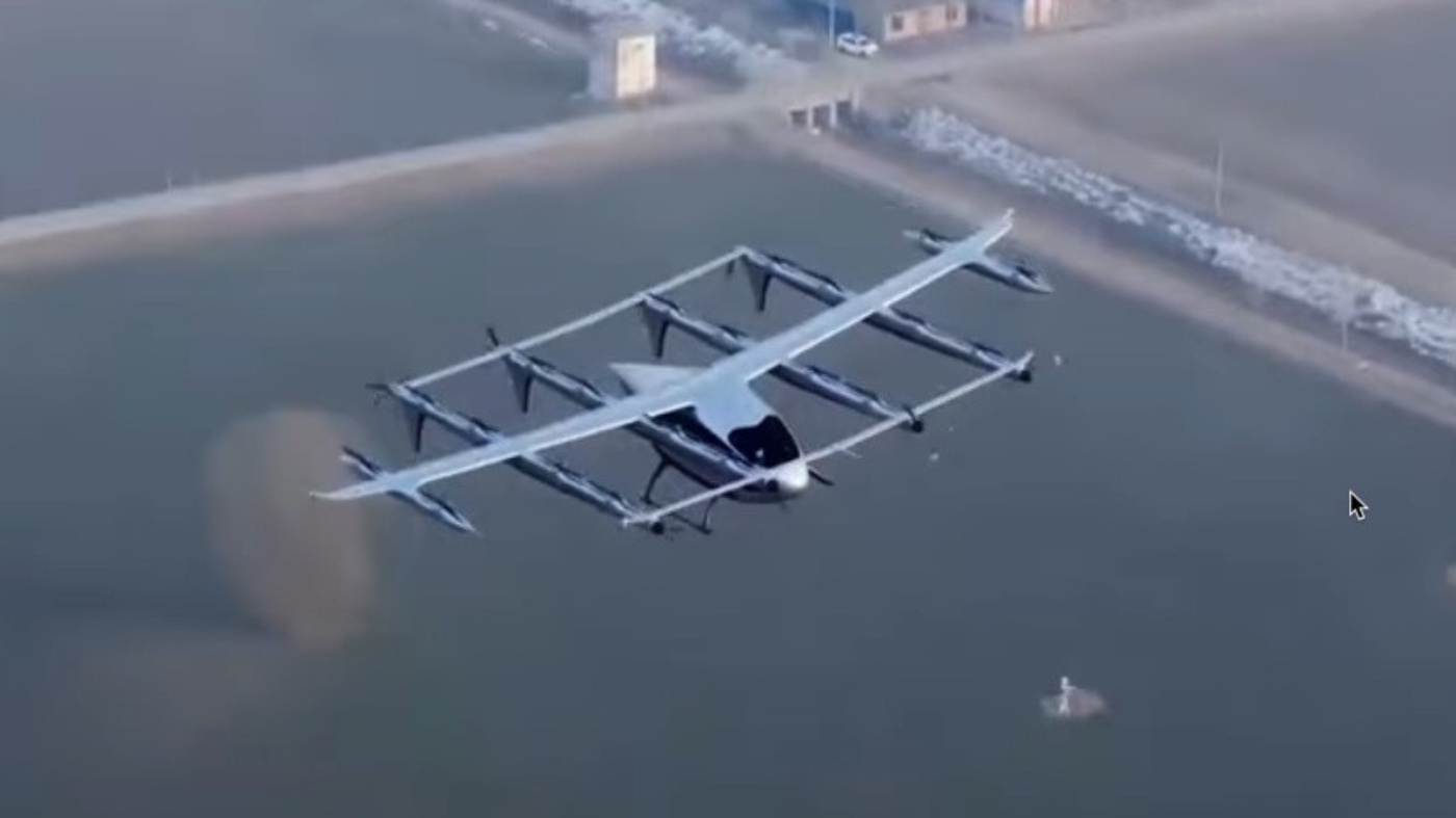 Elektrisches Senkrechtstart-Flugzeug mit mehreren Rotoren fliegt über ländliches Gebiet.
