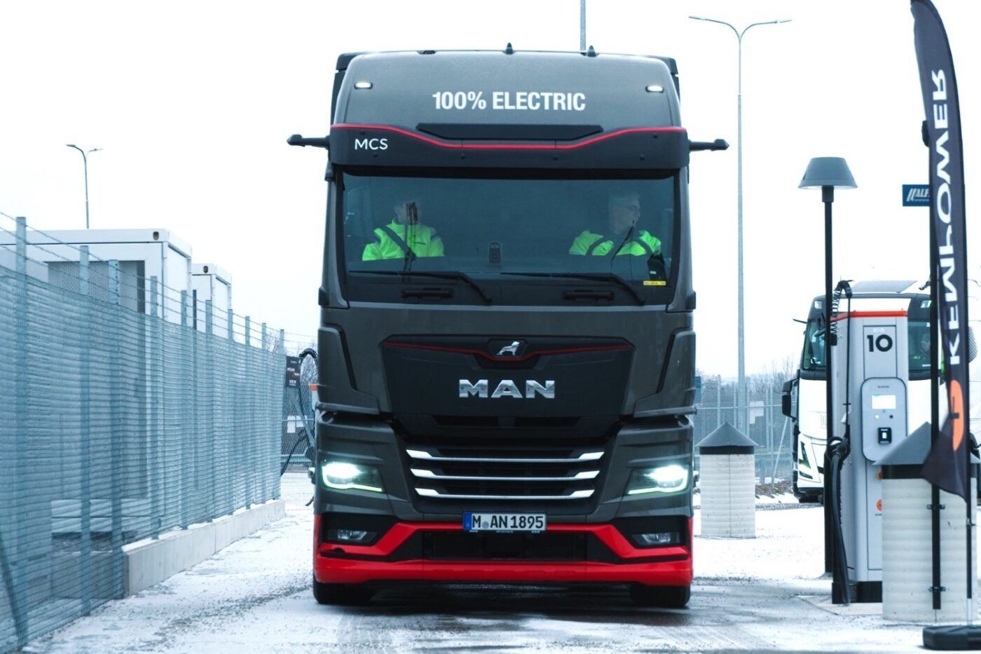Electric MAN truck at a charging station with two people visible in the cab.