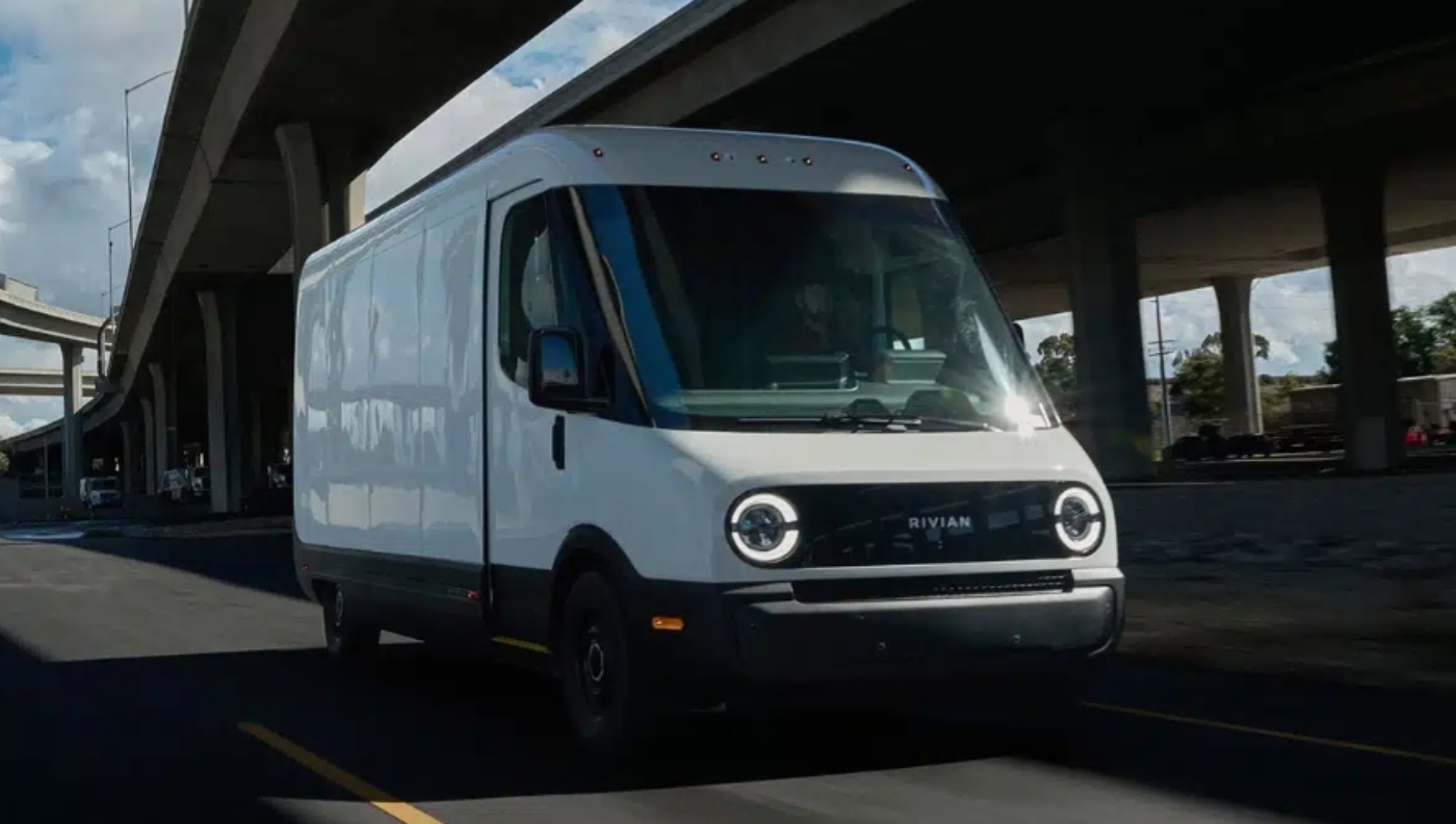 Weißer elektrischer Rivian-Lieferwagen fährt auf einer Straße unter einer Autobahnbrücke.