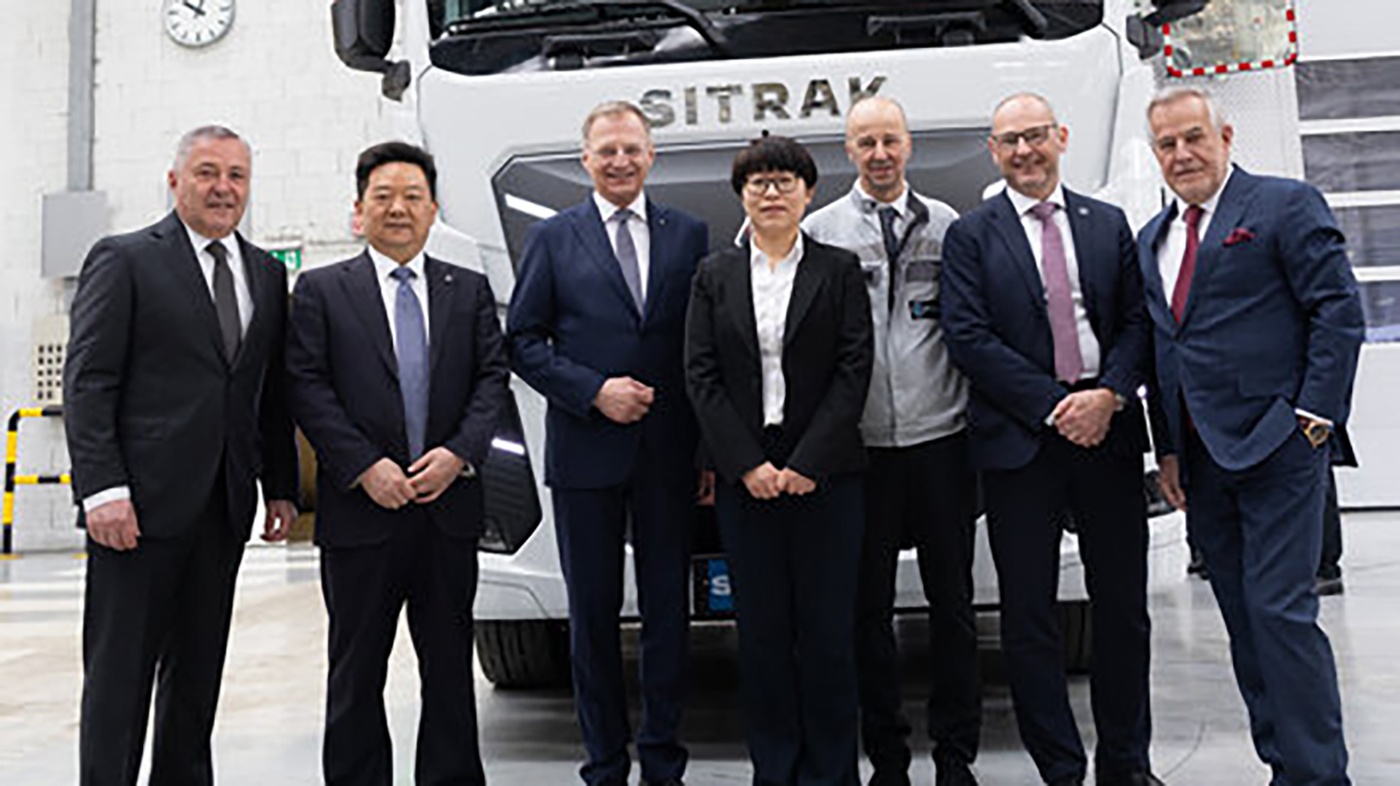 Seven businesspeople stand in front of a SITRAK truck in a factory hall.
