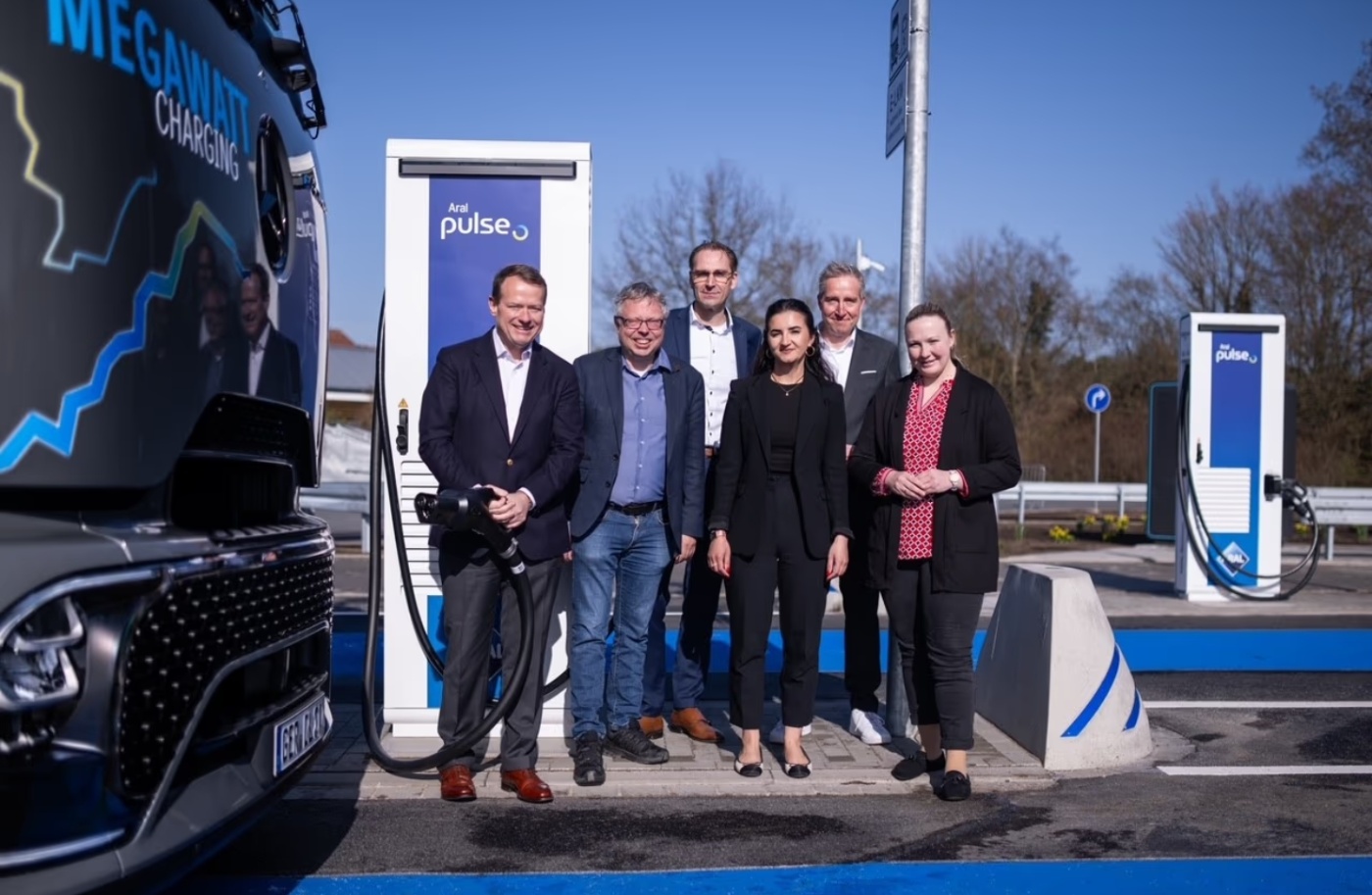 Fünf Männer stehen draußen vor einem Bus und einer E-Ladestation.