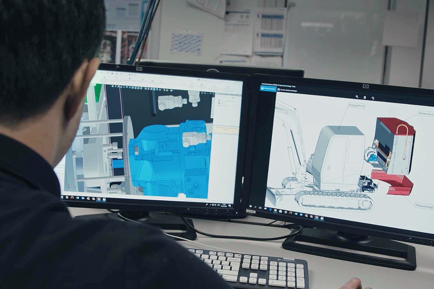 Ein Mann betrachtet zwei technische 3D-Modelle auf Monitoren im Büro.