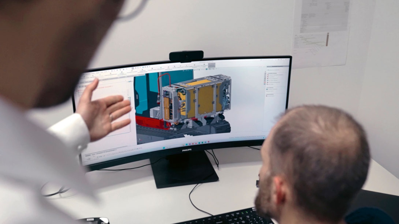 Zwei Männer betrachten ein 3D-Maschinenmodell am Computer im Büro.