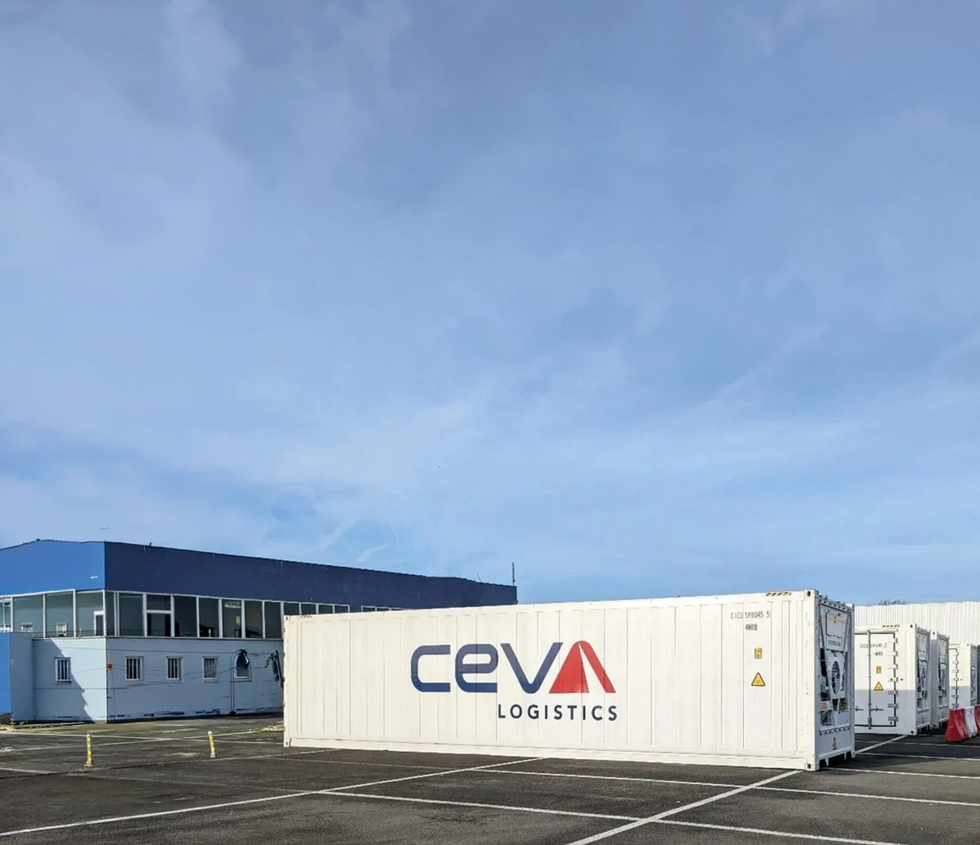 Ein CEVA-Logistics-Container steht im Freien nahe Lagerhalle und Bergen.