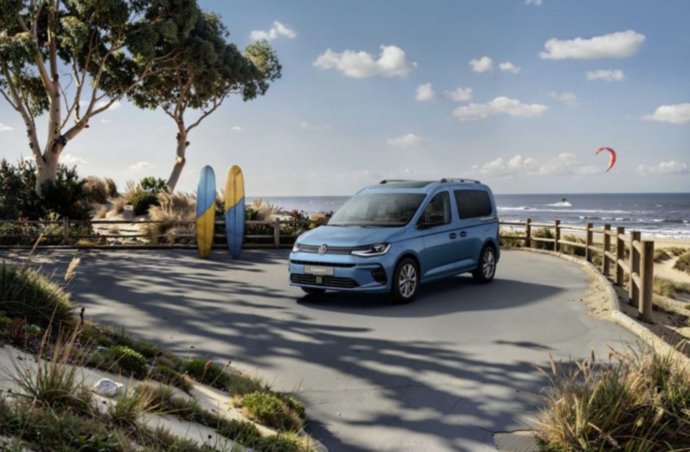 Blue van parked by the beach with surfboards and sea in background