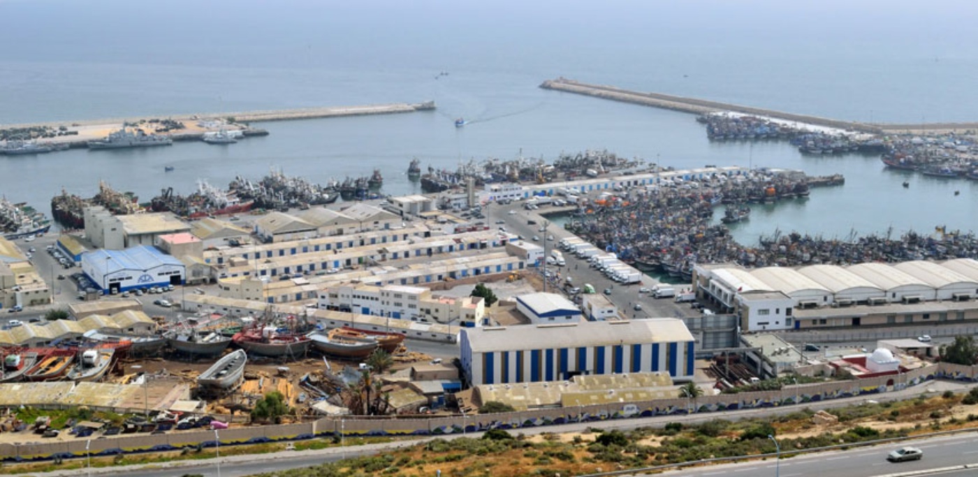 Aerial view of a port with fishing boats and industrial buildings by the sea.