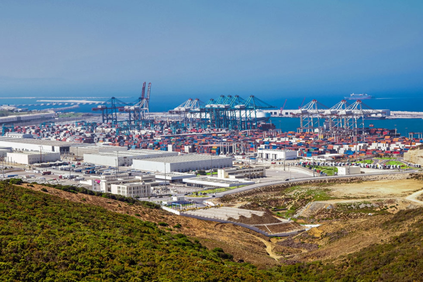 Großer Containerhafen mit Kränen und gestapelten Containern am Meer.