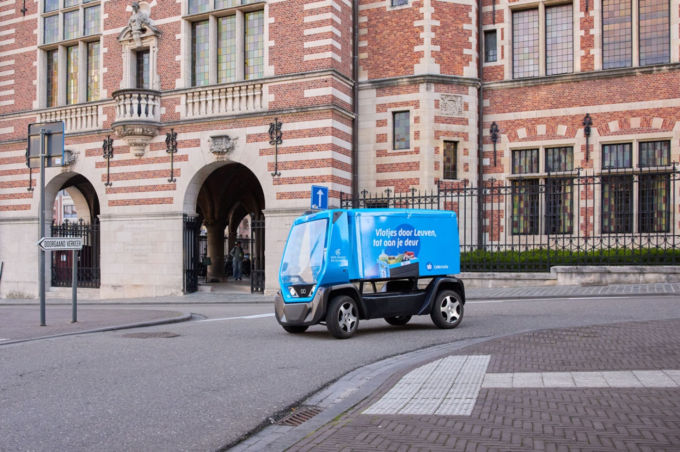Small blue electric waste vehicle driving in front of a historic building.