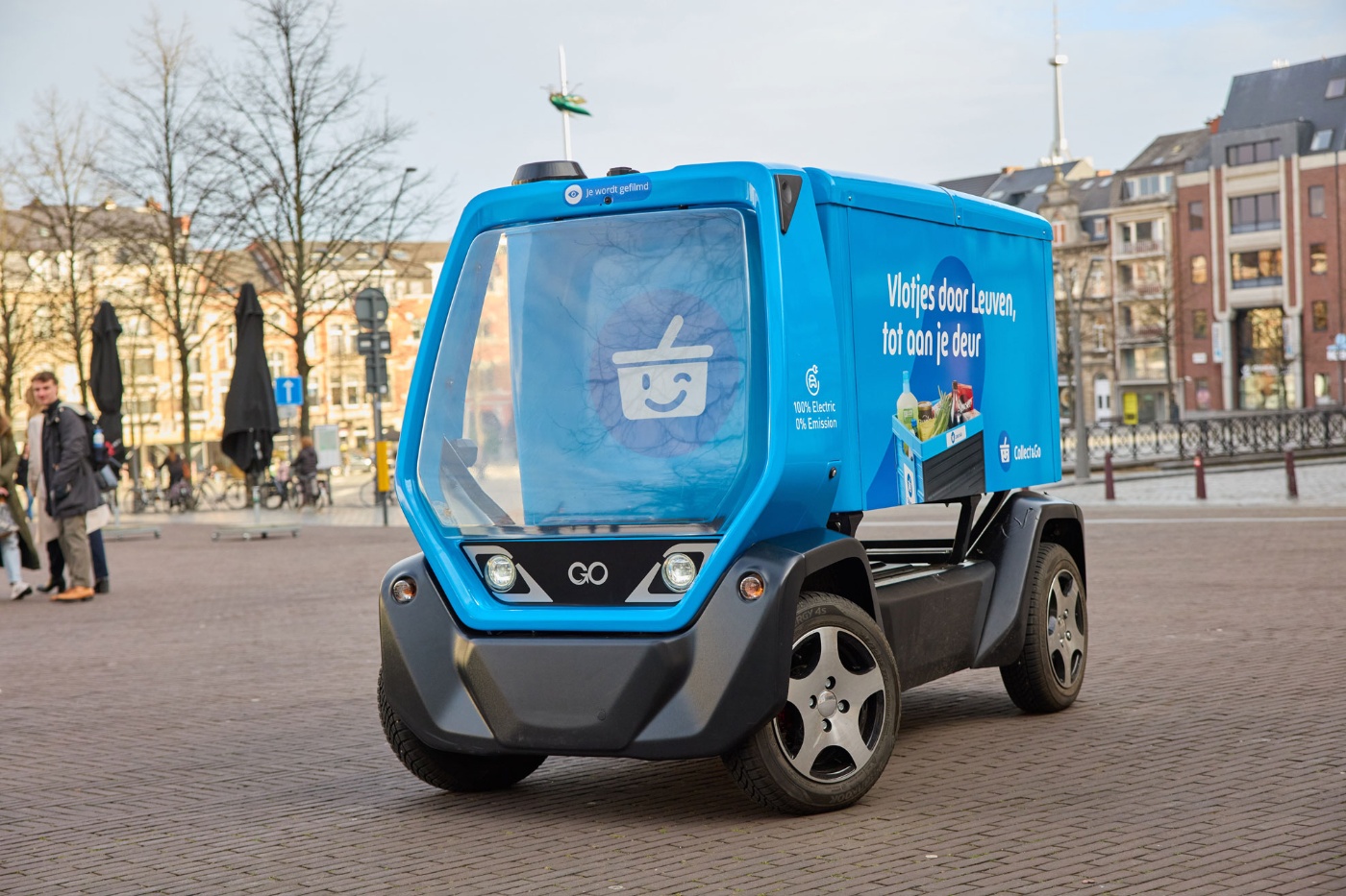 Small blue electric waste vehicle parked on a cobblestone city square.