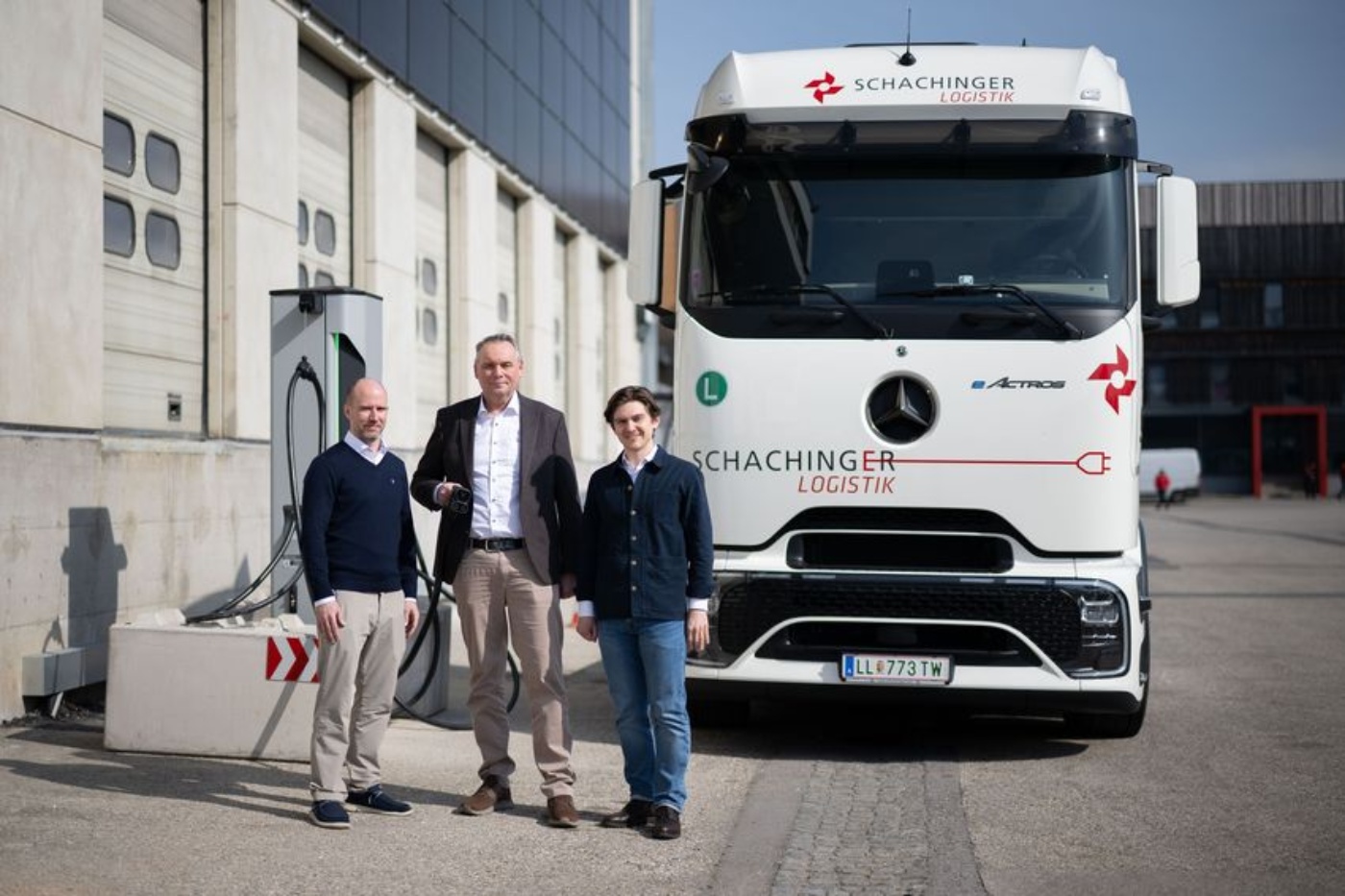 Drei Männer stehen vor einem weißen Lkw vor einem Industriegebäude.