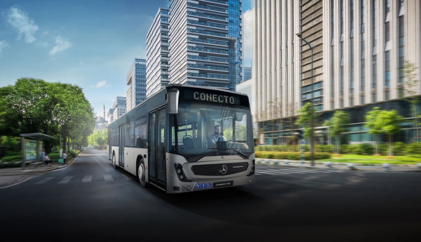 Moderner Stadtbus fährt auf breiter Straße zwischen hohen Bürogebäuden.