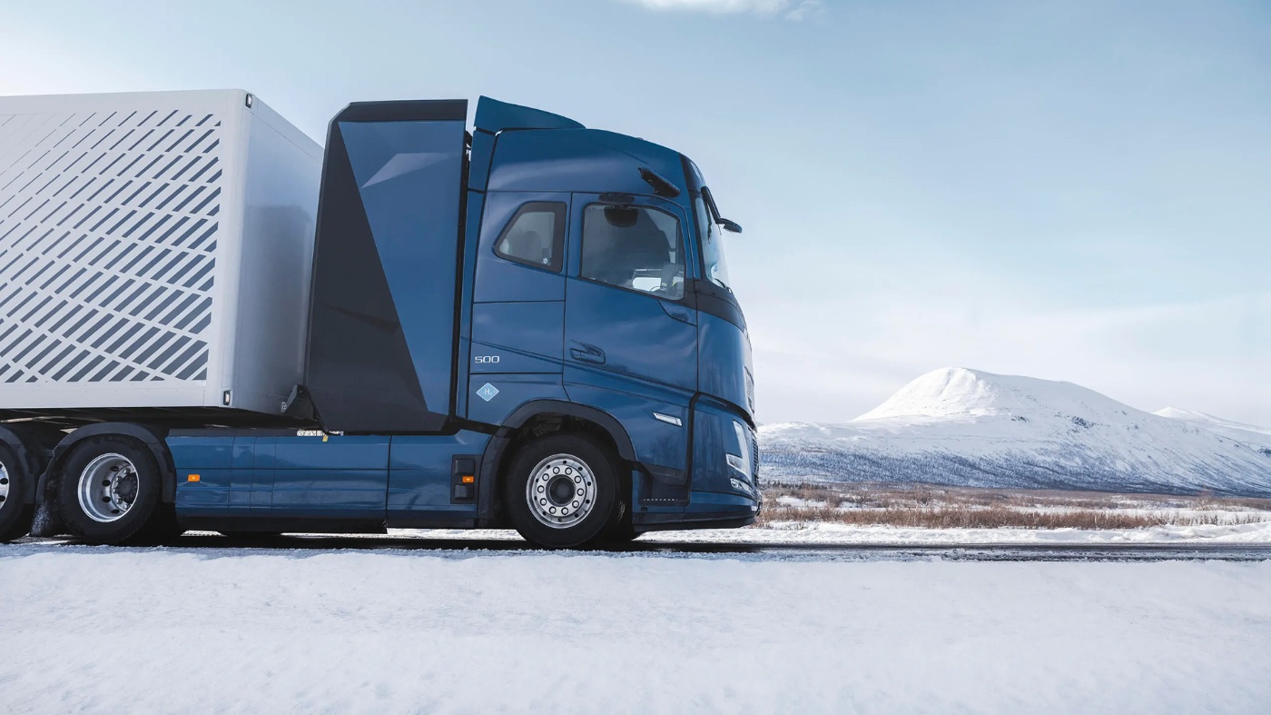 Volvo truck driving on a snowy road with mountains in the background.