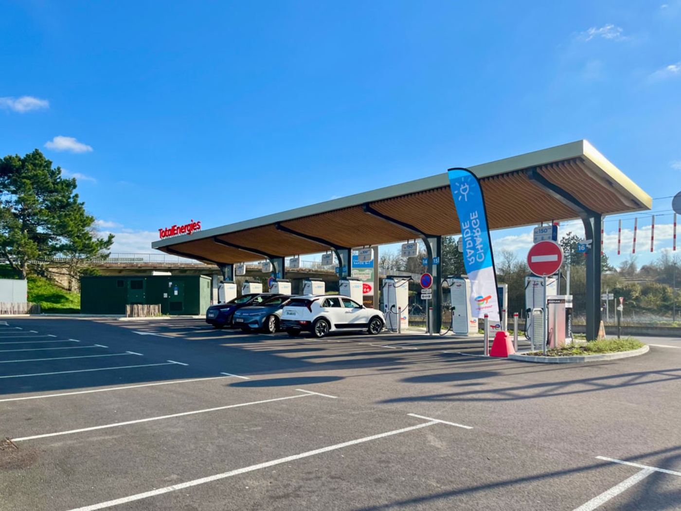 Electric cars charging at a TotalEnergies station under a large roof.