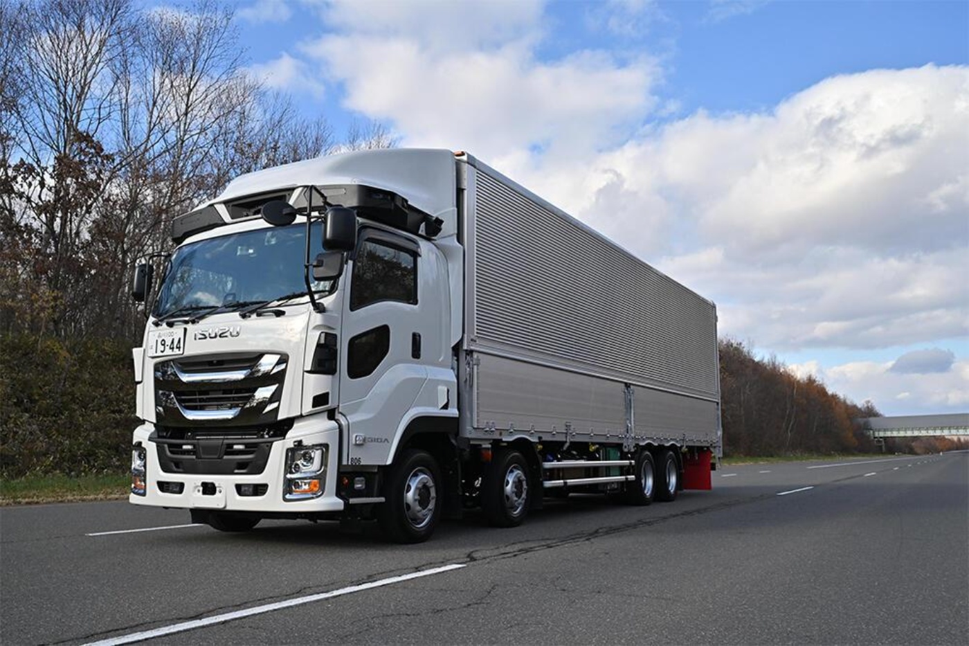 White semi-truck with trailer driving on a highway under a cloudy sky.