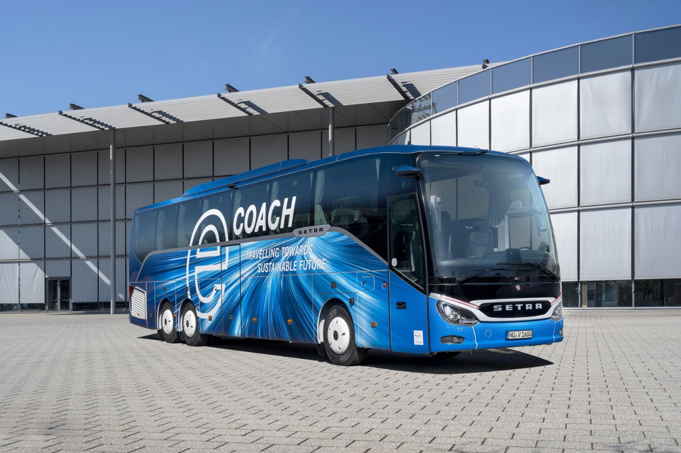 Blue Setra coach with sustainability slogan parked in front of a modern building.