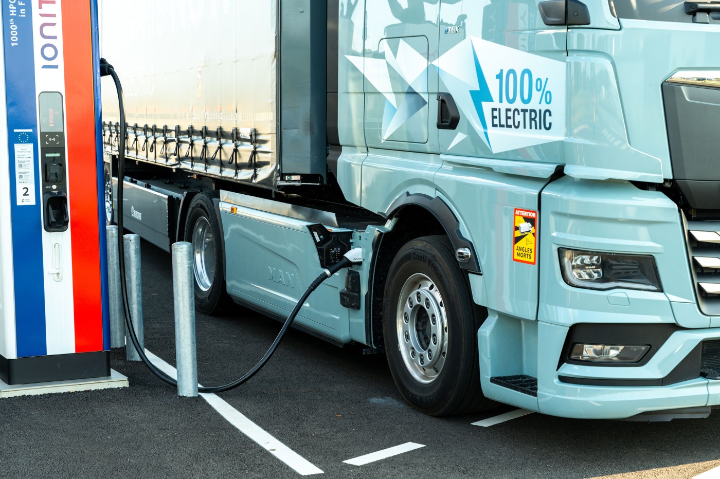 Electric truck charging at a public station, labeled 100% electric.