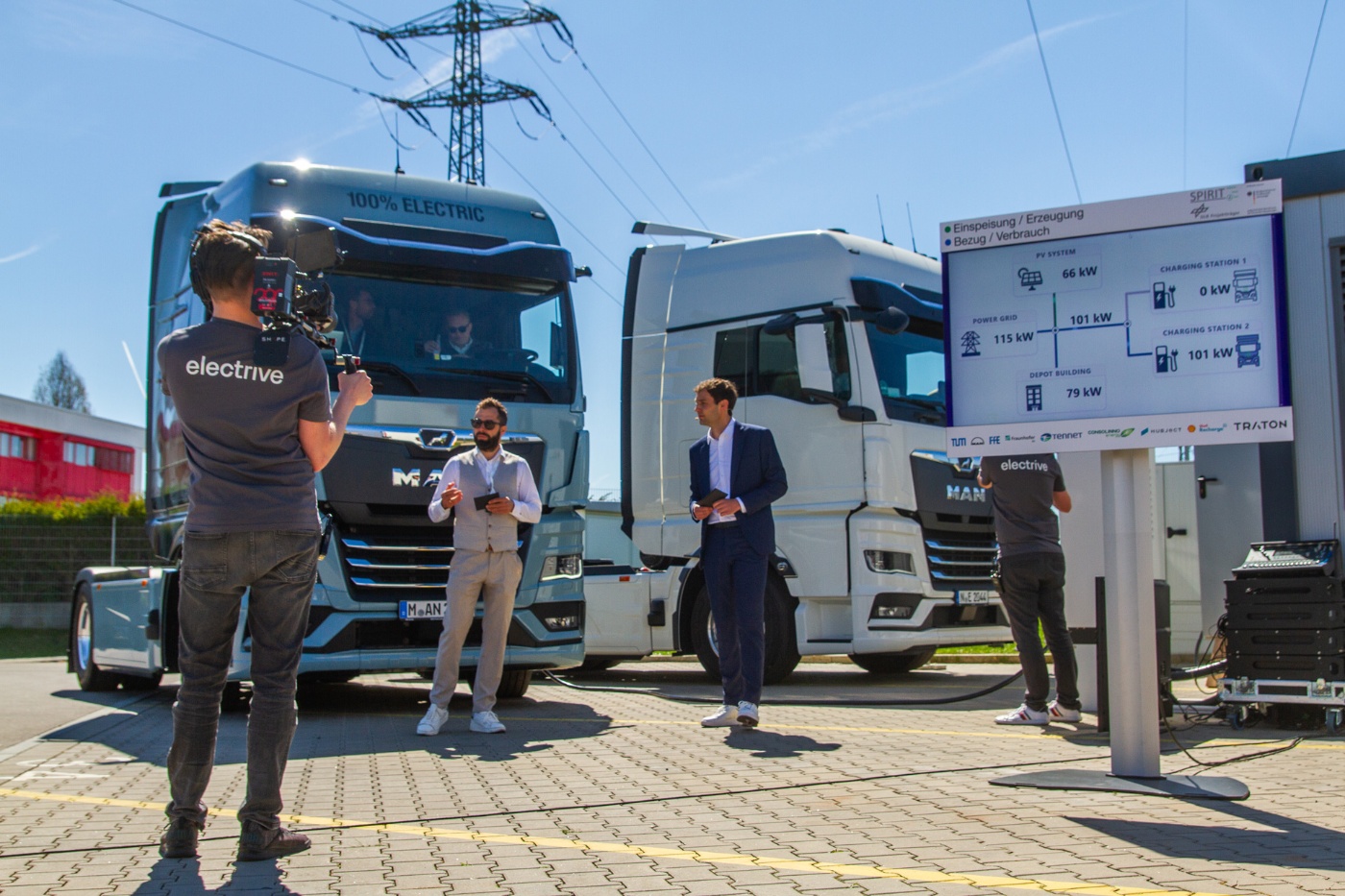 Drei Männer stehen vor MAN Lkw neben einer Infotafel im Freien.
