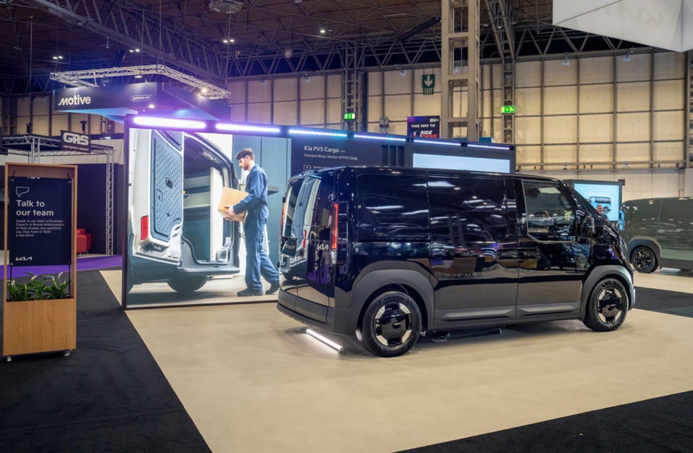 Kia PV5 Cargo Transporter auf einem Messestand mit großer Leinwand.