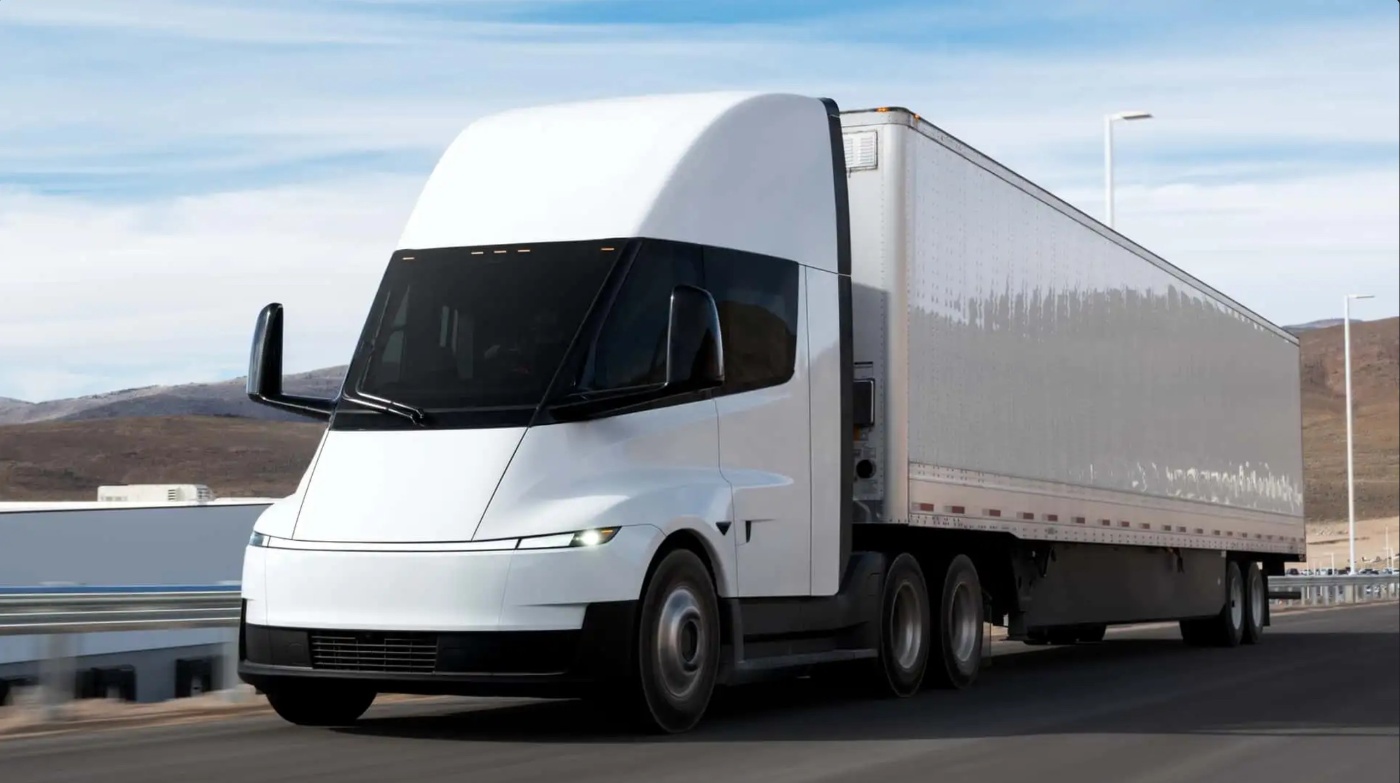 Electric semi-truck driving on a highway in a rural landscape.