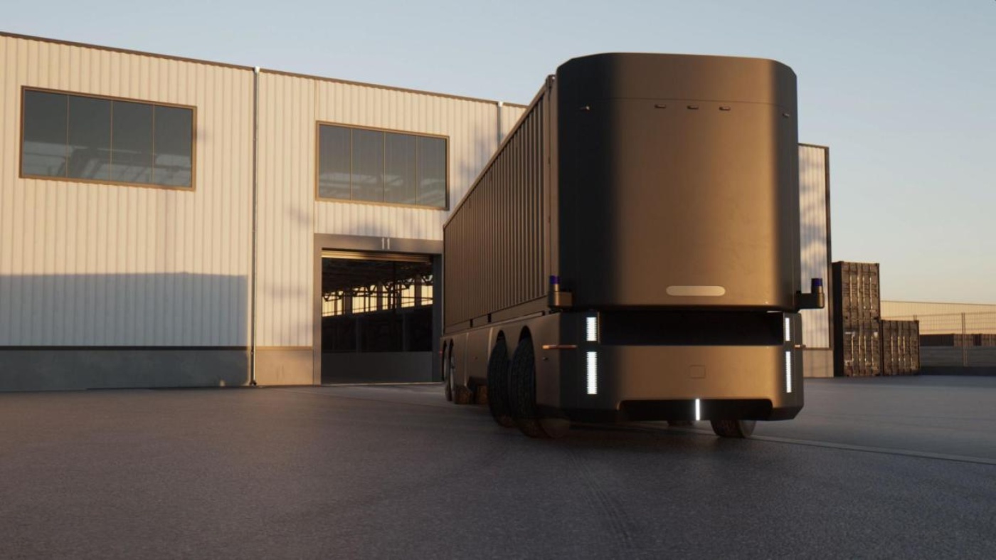 Autonomous electric truck in front of a warehouse building.
