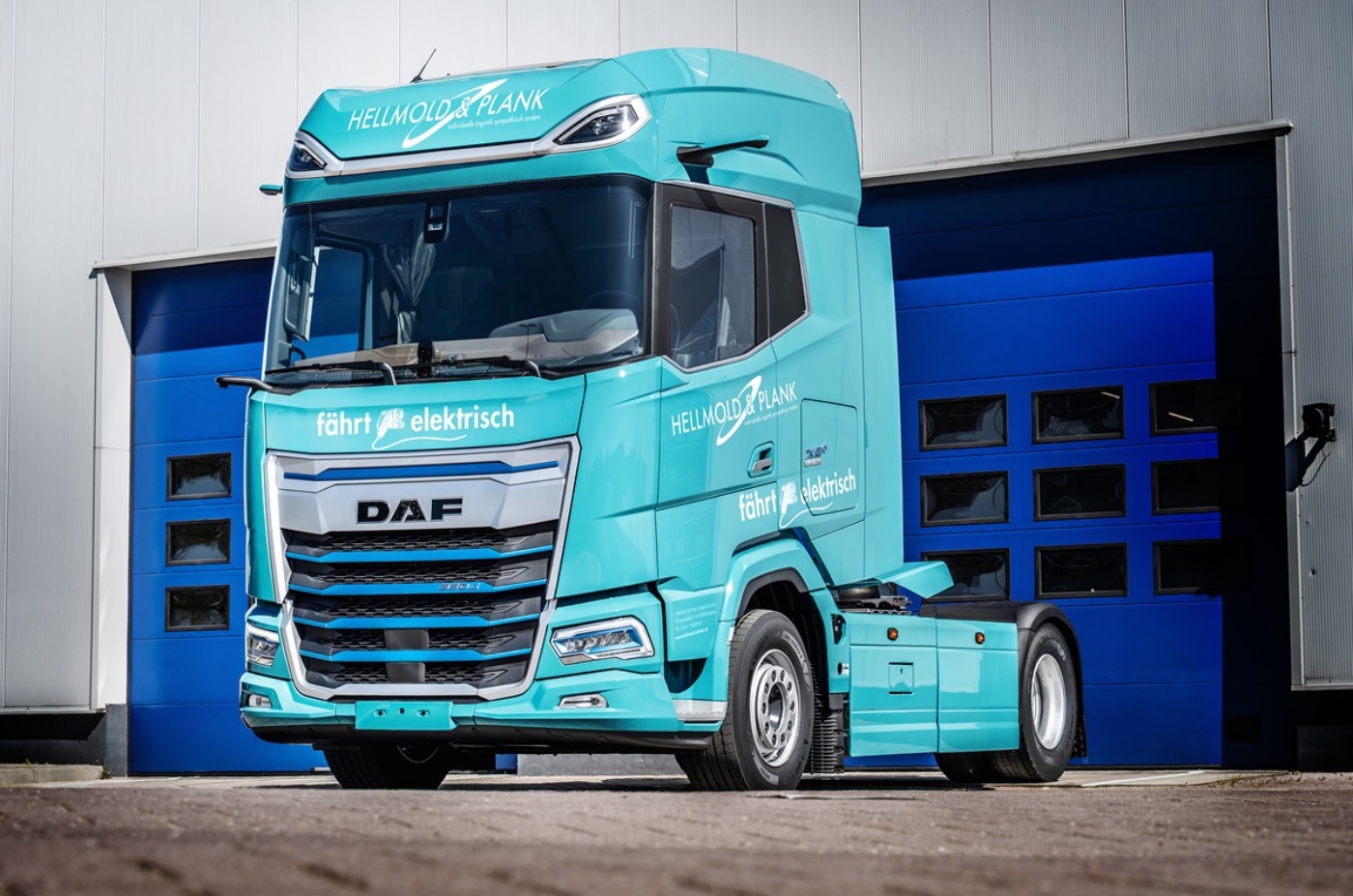 Turquoise DAF electric truck with Hellmold & Plank branding in front of a warehouse.