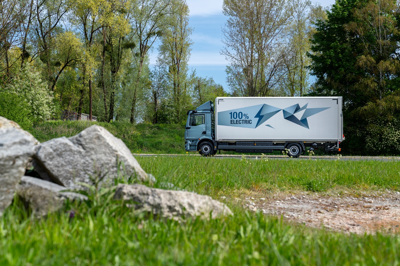 MAN electric truck with “100% Electric” label driving past trees.