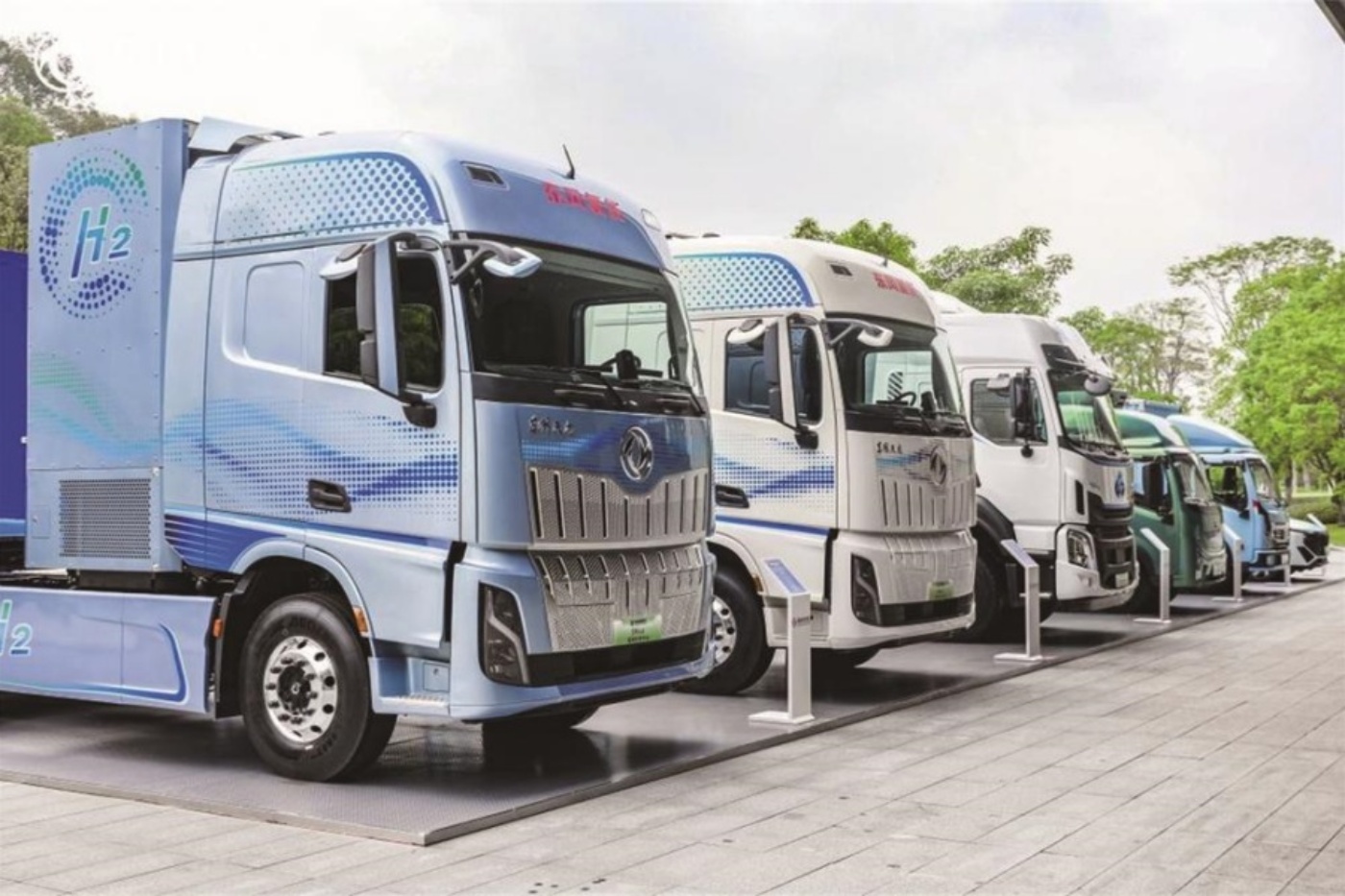 Row of hydrogen trucks labeled H2 parked outdoors at a display area.