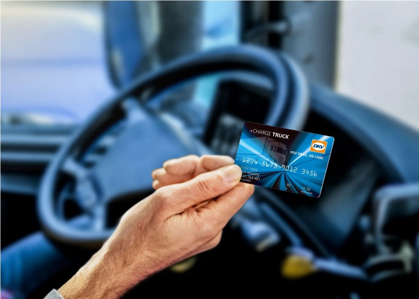 Driver holding a DKV Charge Truck card inside a truck cabin.