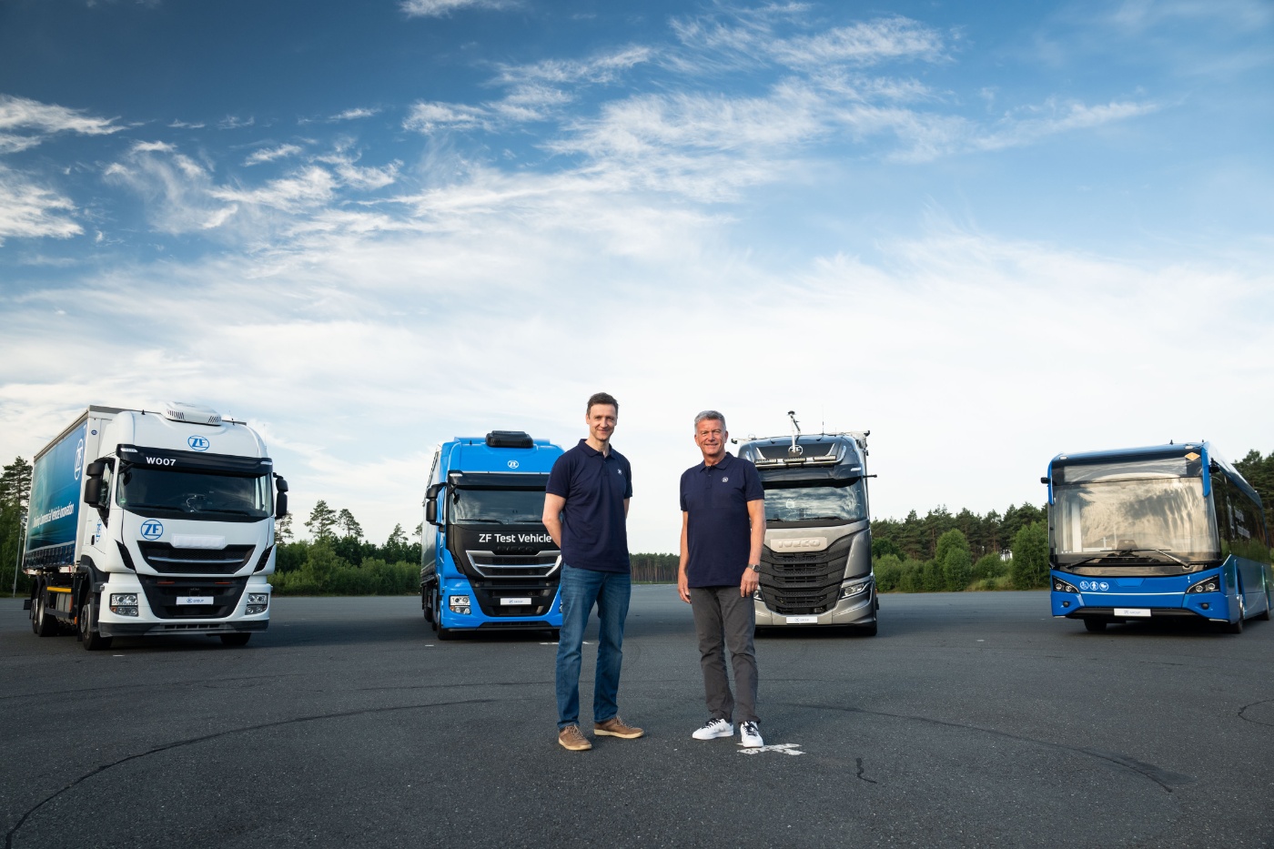 Two people stand between ZF test trucks and a bus on a test facility.
