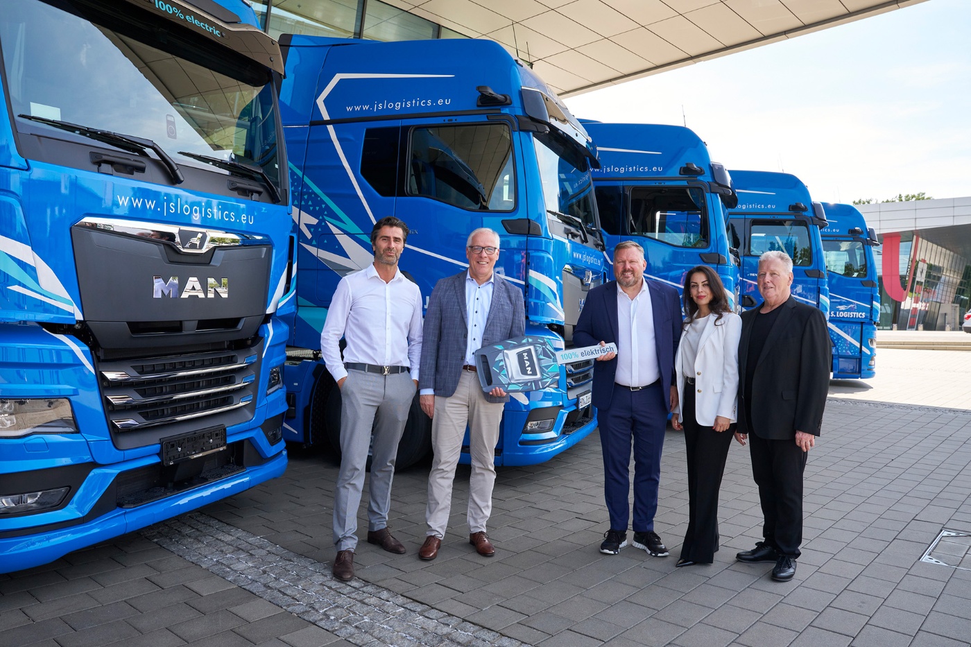 Fünf Personen stehen vor blauen Elektro-Lkw von J.S. Logistics.
