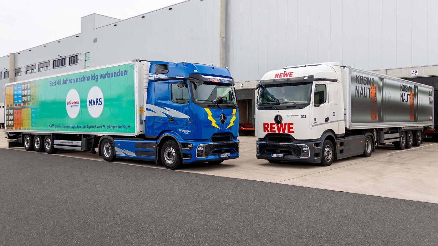 Zwei Marken-Lkw stehen nebeneinander an einer Laderampe vor einem Lagergebäude.