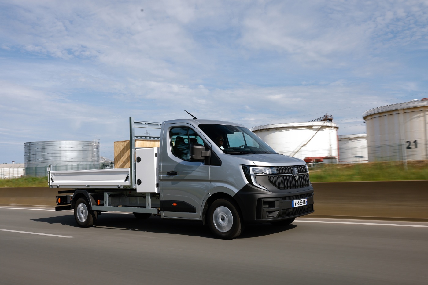 Grey Renault flatbed truck driving on a road in an industrial area.