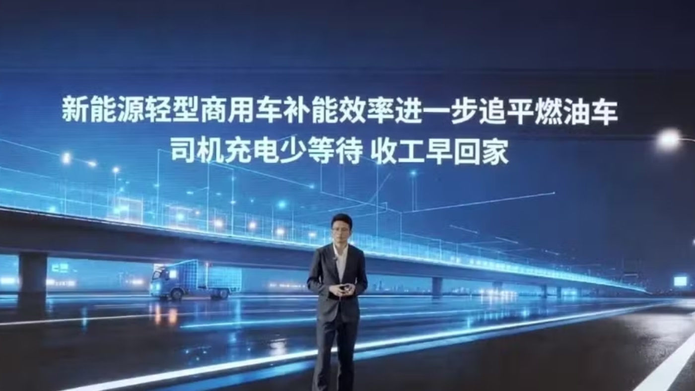 Presenter on a stage in front of a screen with Chinese text and a night city backdrop.