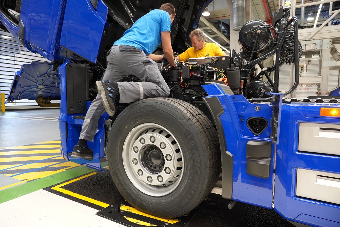 Mitarbeiter montiert ein Rad an einem blauen MAN-Lkw in der Fahrzeugmontage.