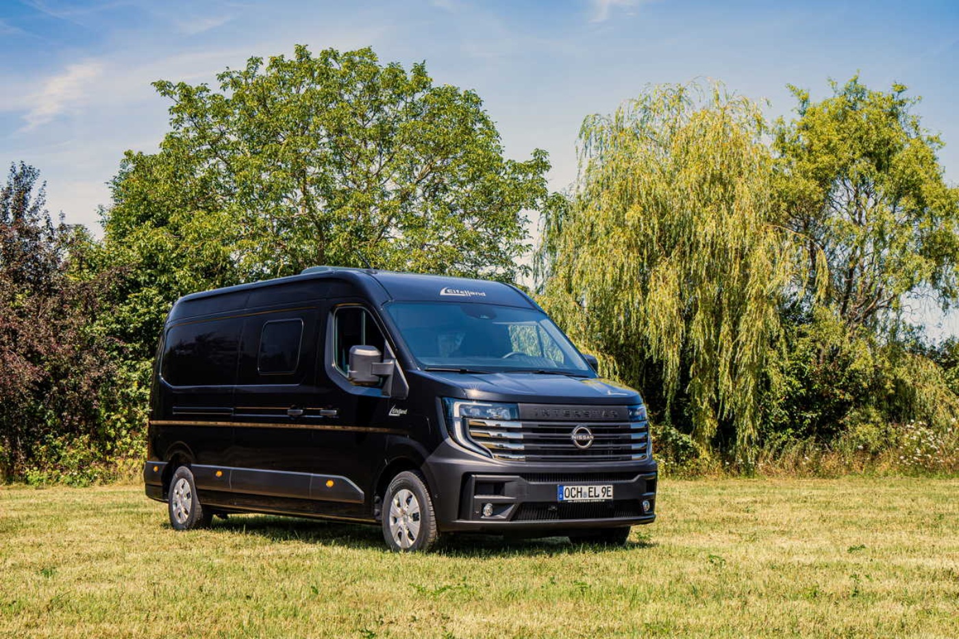 Nissan electric van parked on a grassy field with trees in the background.