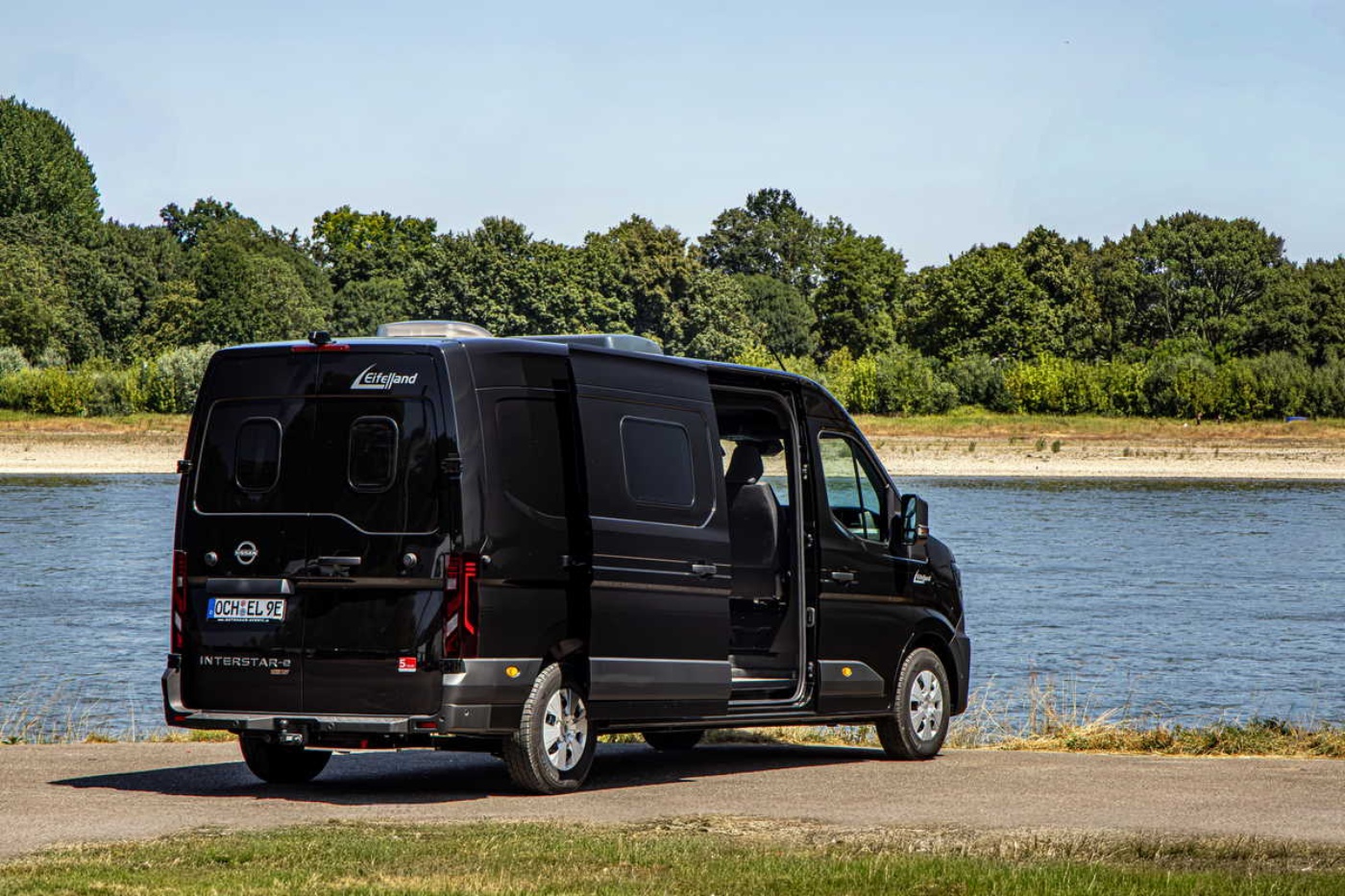 Elektrischer Nissan-Transporter steht am Wasser mit geöffneter Schiebetür.