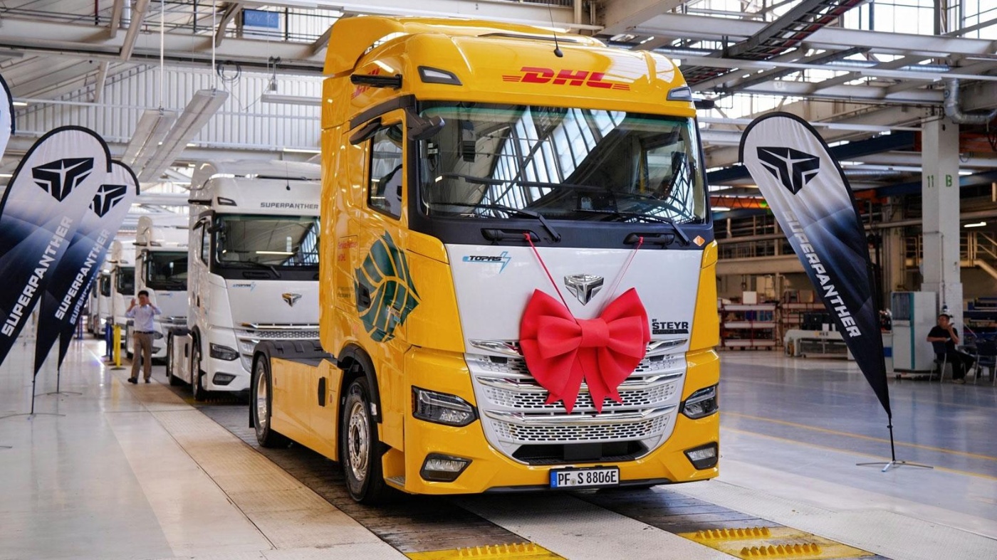 DHL electric truck with a red gift bow displayed inside a production hall.