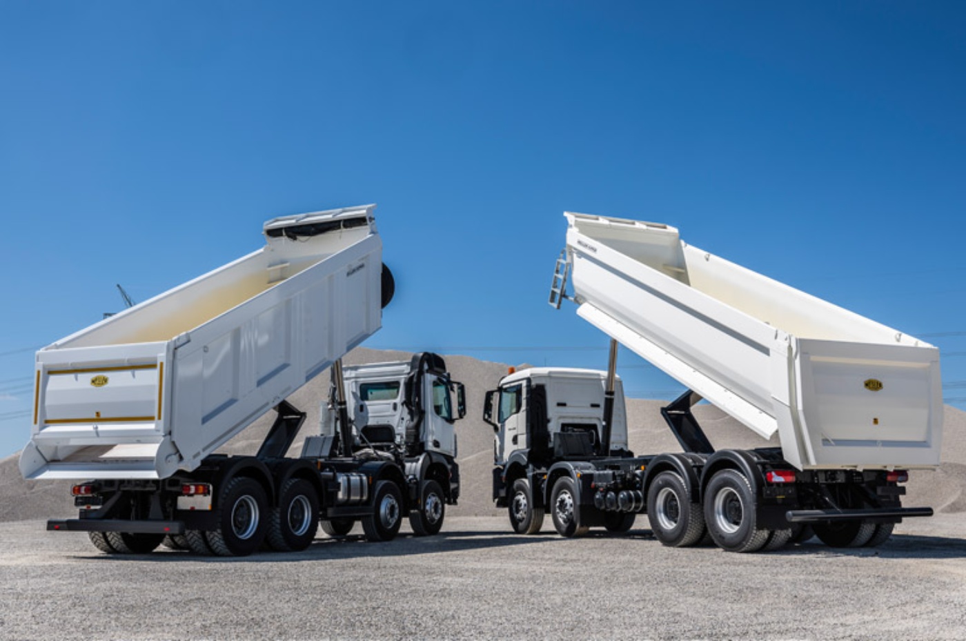 Two Meiller tipper trucks with raised dump beds parked side by side.