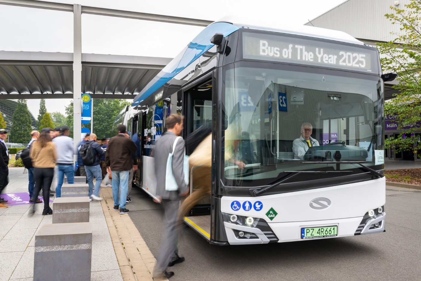 Shuttlebus an einer Messehaltestelle, während Besucher einsteigen.