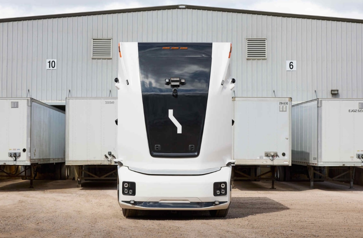 Autonomer Elektro-Lkw von Einride vor einer Lagerhalle mit Anhängern.
