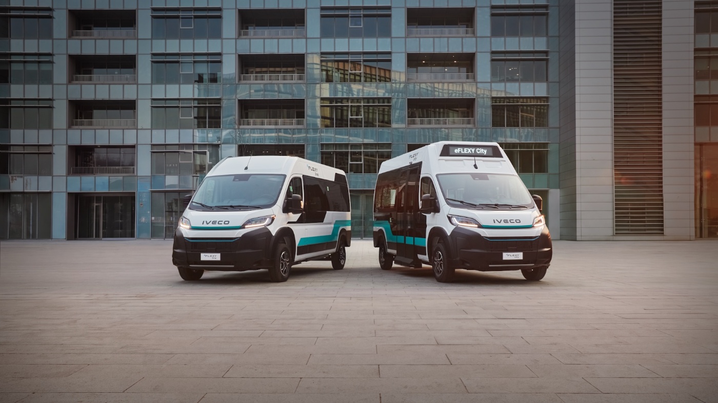 Two IVECO eFLEXY minibuses stand in front of a modern building.